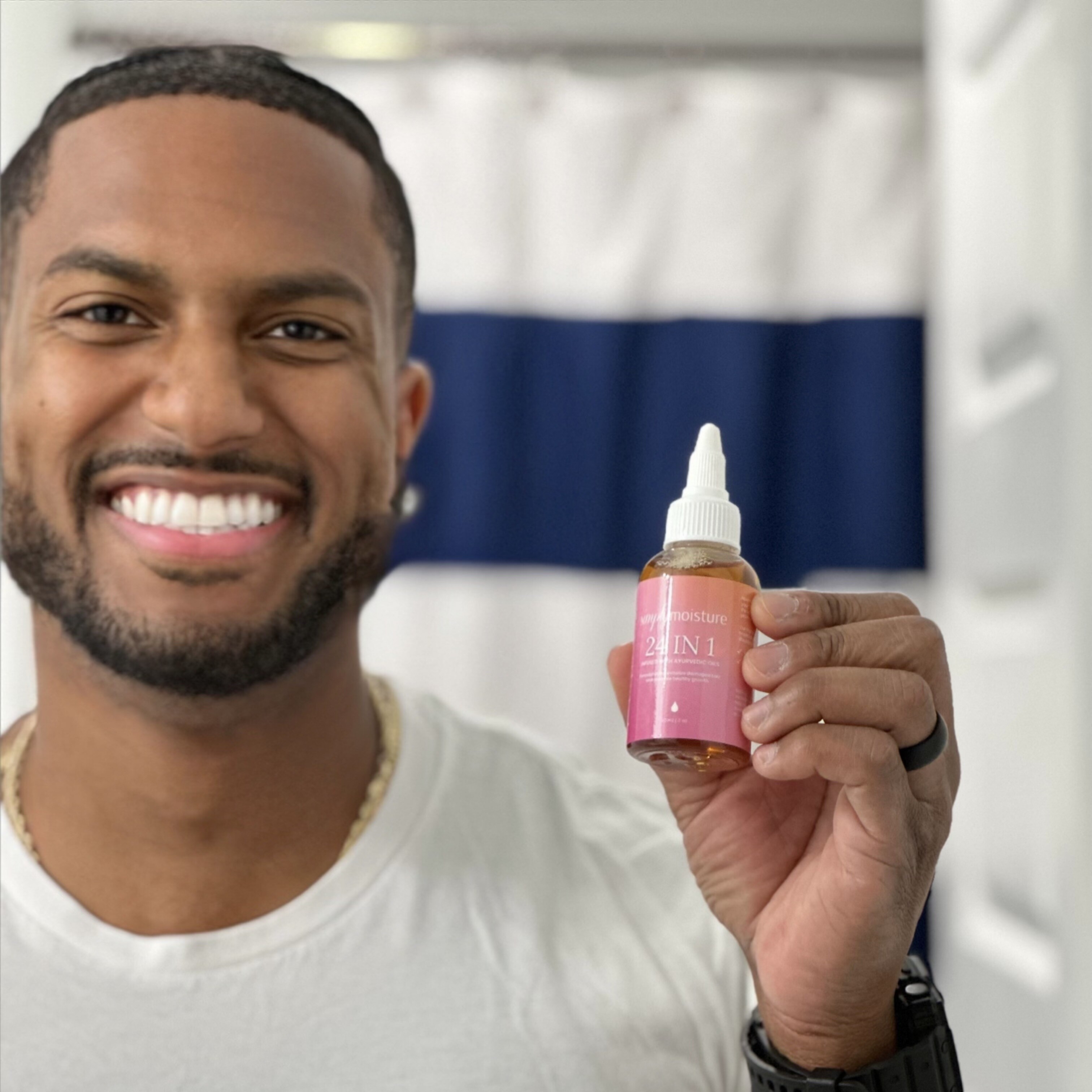 Smiling person holding a bottle of hair product in a bathroom.