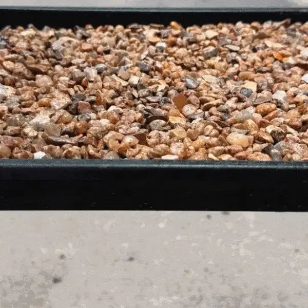 A close-up video of a black tray filled with small pebbles that are being shaken.