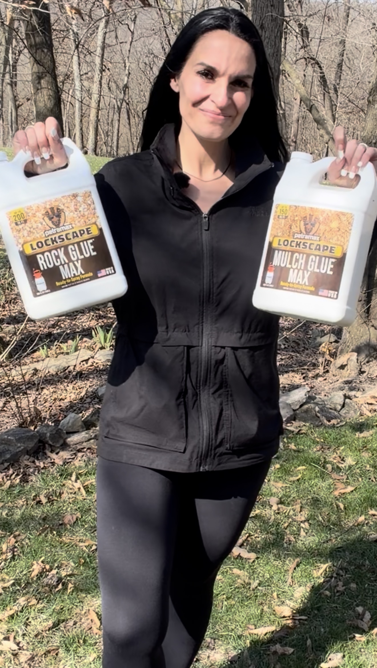 A woman in a black jacket stands outside holding two jugs of Lockscape glue.