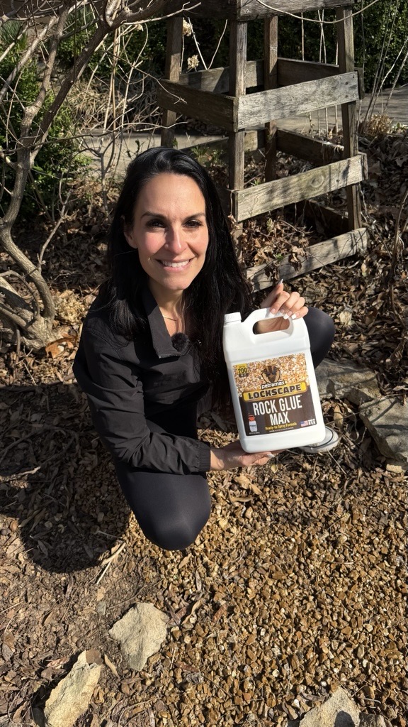 A woman kneels outdoors on a gravel path, holding a bottle of Lockscape Rock Glue Max.