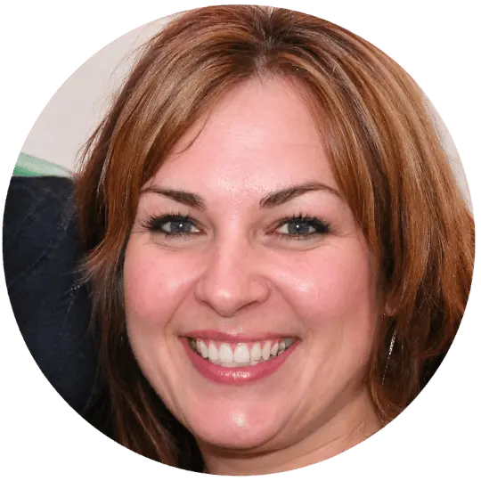 A circular headshot of a smiling woman with light brown hair and blue eyes.