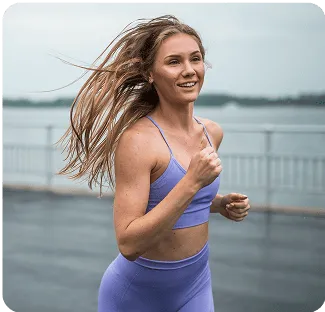 Person jogging outdoors near a waterfront, wearing purple workout attire.