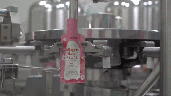 Pink bottle labeled 'collagen glow berries' on a production line.
