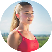 A woman with a blonde ponytail in a pink top, looking to her right outdoors.