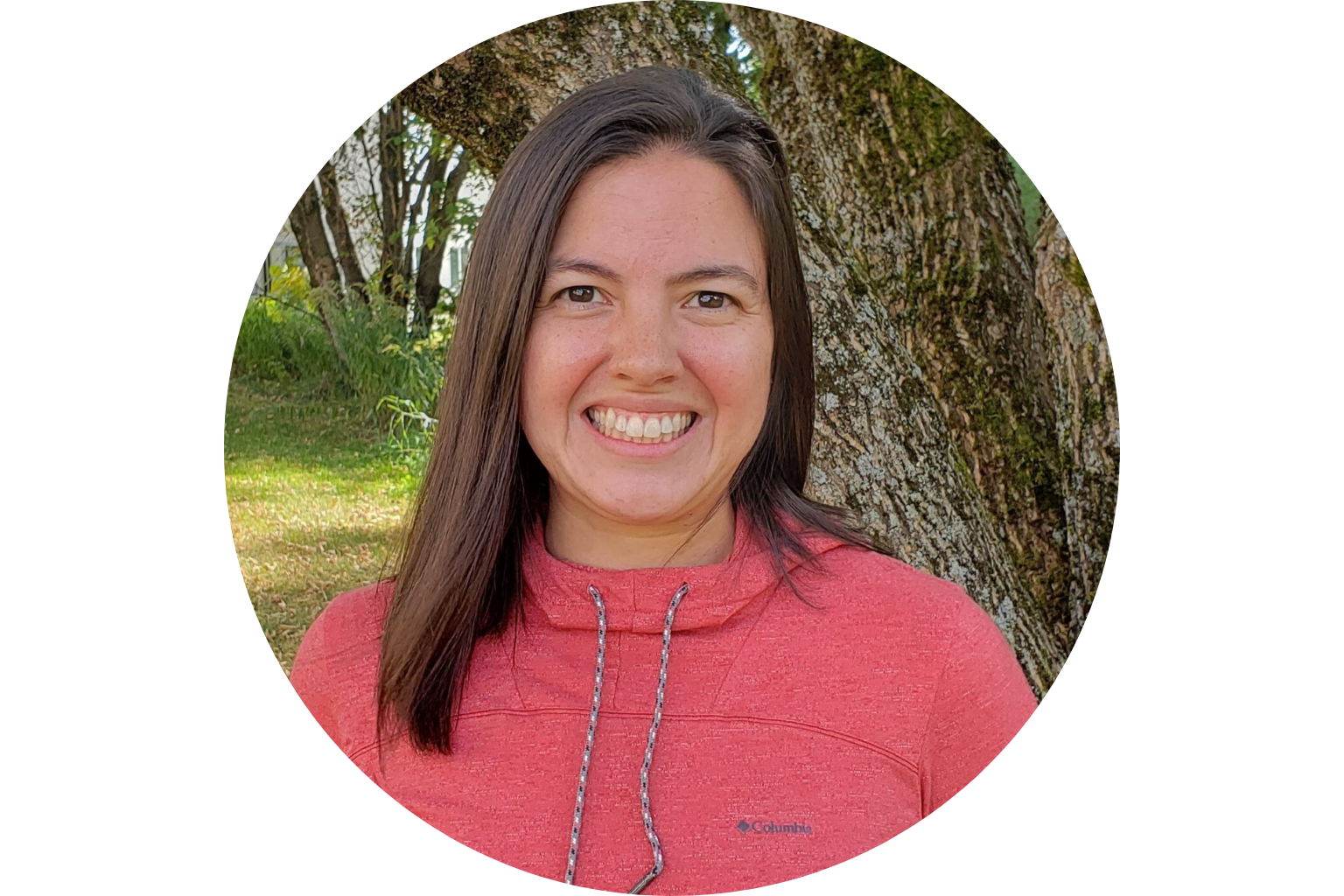 Smiling person in a red hoodie standing outdoors near a tree.