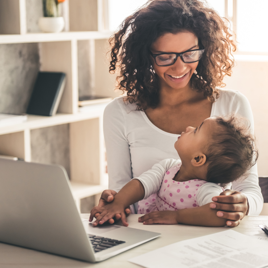 Woman with glasses holding a baby near a laptop, both smiling.