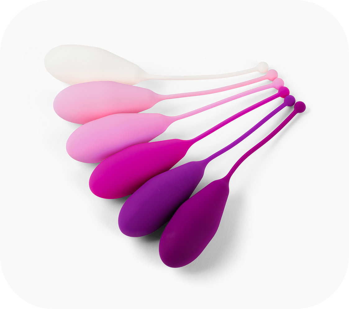 A row of six egg-shaped silicone Kegel balls with tails, in a gradient of white, pink, and purple.