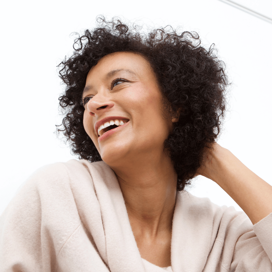 A person with curly hair smiling and looking to the side.