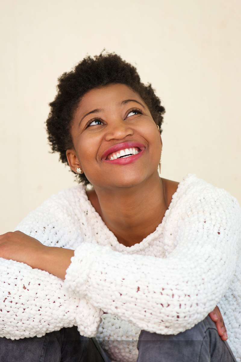 Smiling person looking upwards, wearing a white sweater.