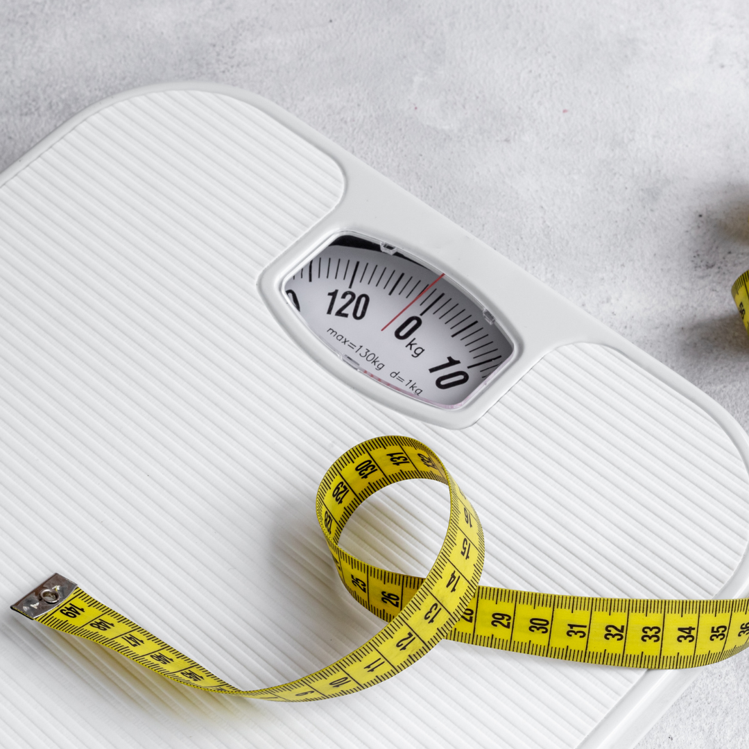 White bathroom scale with a yellow measuring tape on a gray surface.