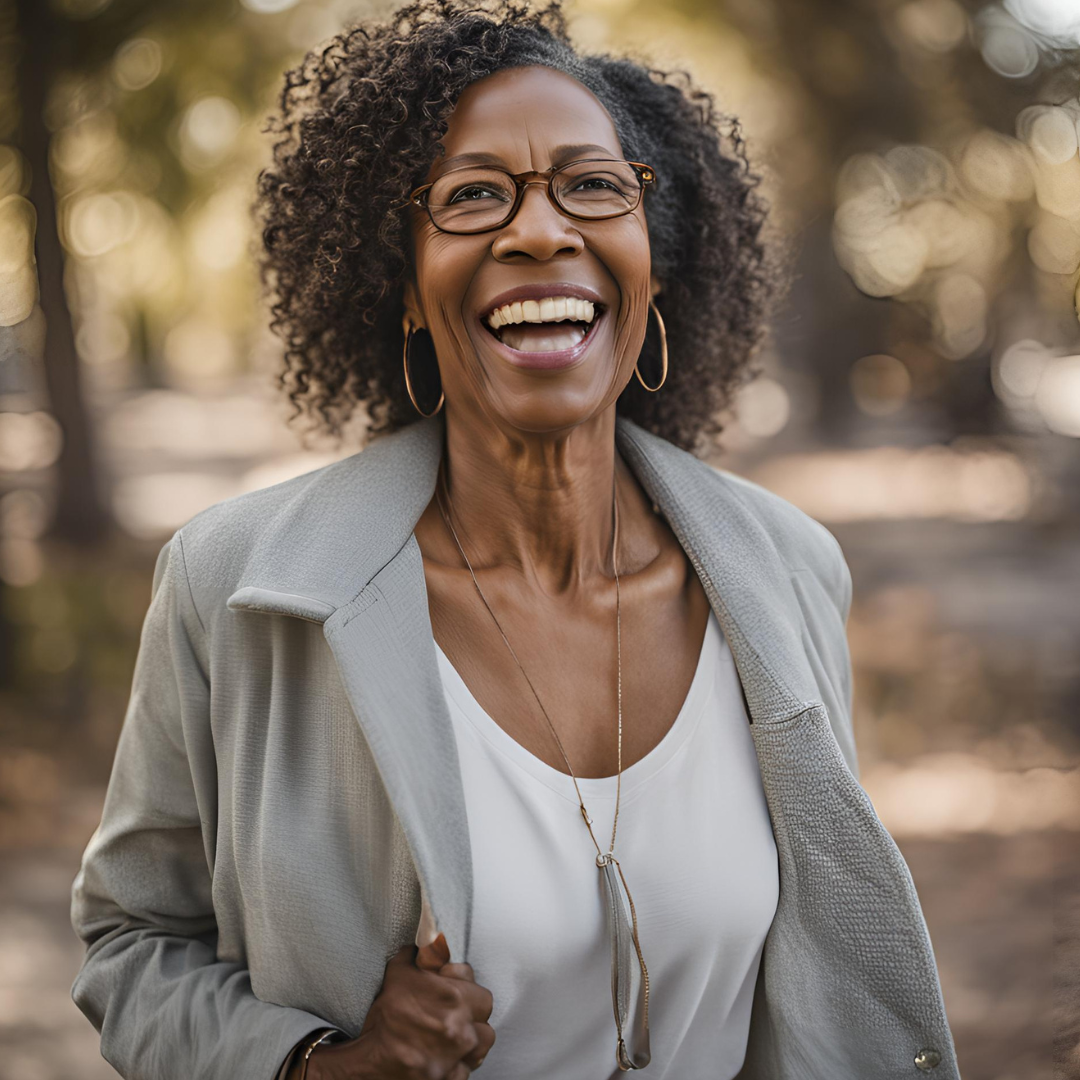 Smiling person with glasses and curly hair, wearing a gray jacket outdoors.