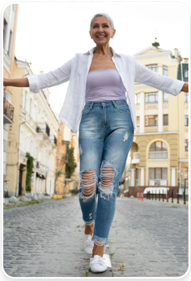 Smiling person walking on a cobblestone street, wearing a white shirt and ripped jeans.