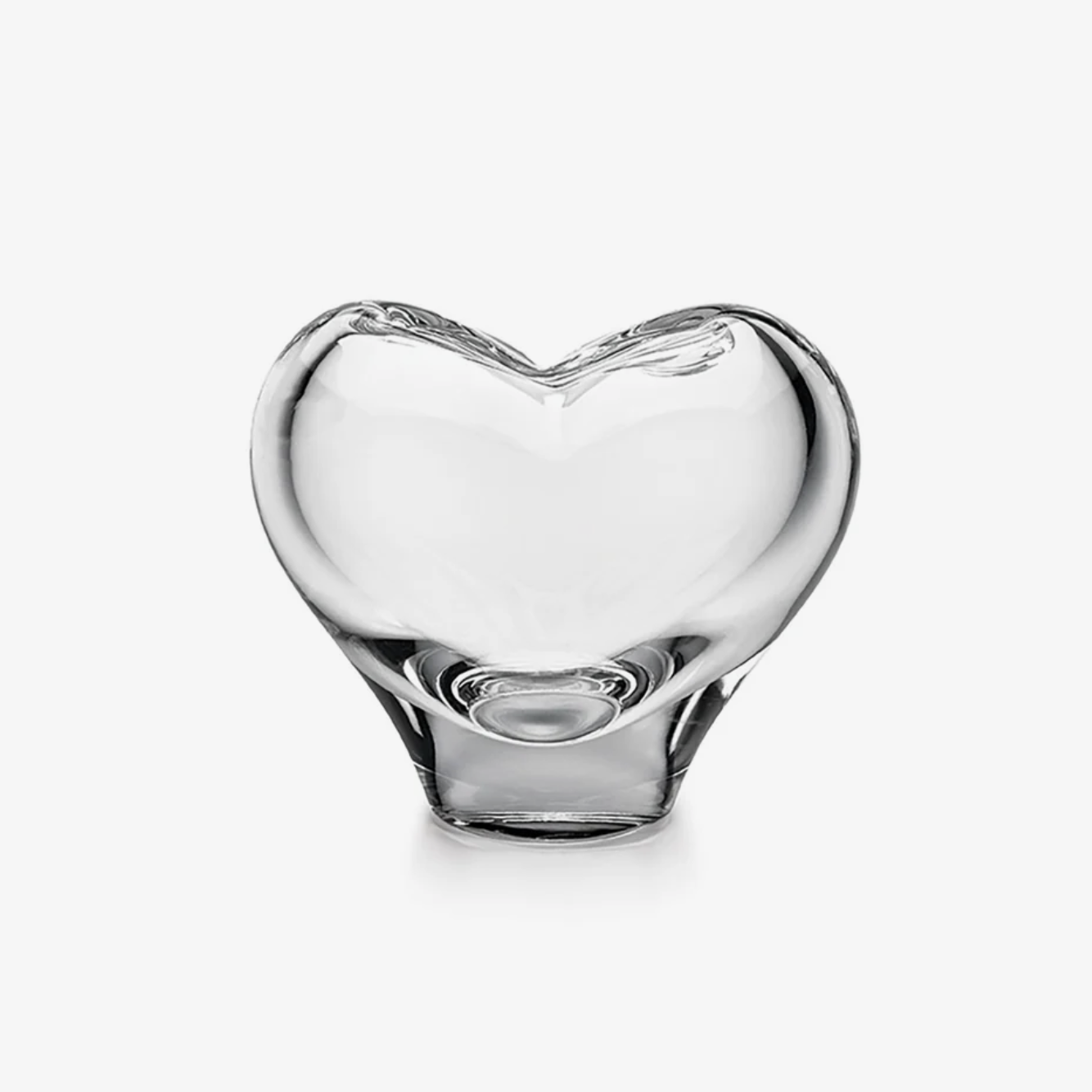 A clear, heart-shaped glass vase or bowl sitting on a white surface against a white background.