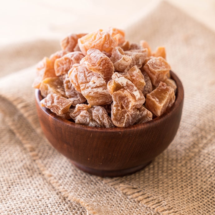 A wooden bowl filled with dried apricots on a burlap cloth.