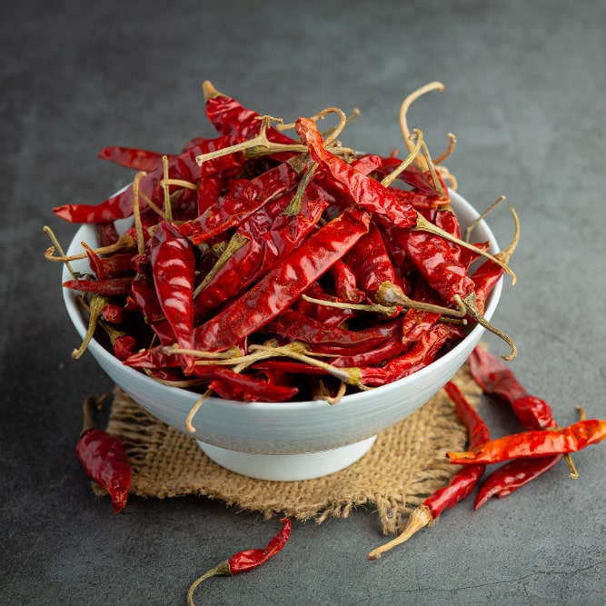 A bowl filled with dried red chili peppers on a burlap mat.