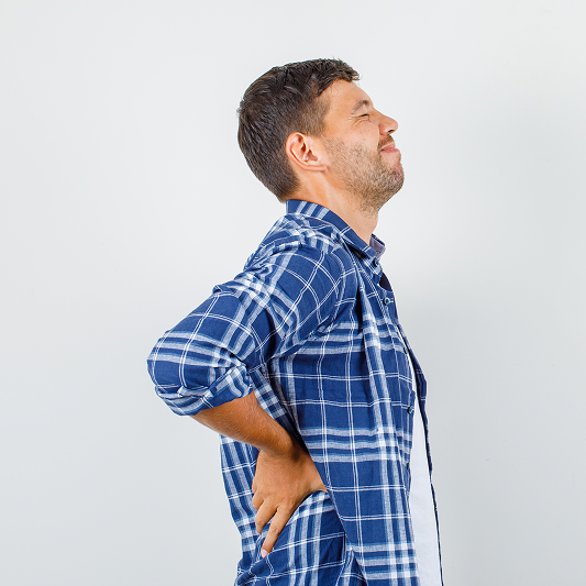 Man in plaid shirt holding his lower back, appearing in discomfort.