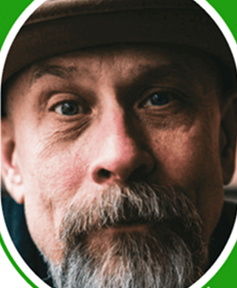 Close-up of a man with a beard and hat, looking directly at the camera.