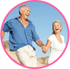 Elderly couple holding hands and laughing on a sunny beach.