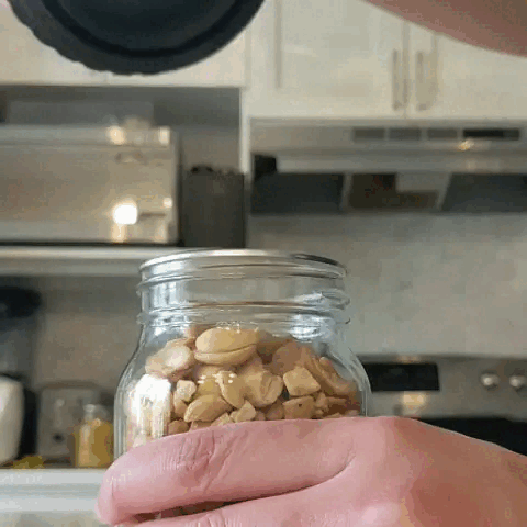 Hand holding a jar of nuts in a kitchen setting.