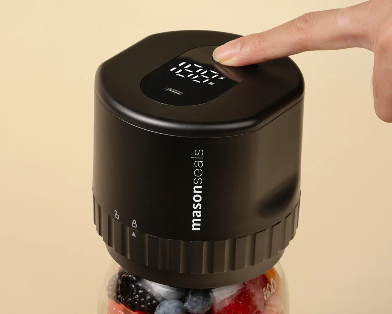 A finger pressing a button on a black mason jar lid with fruit inside.