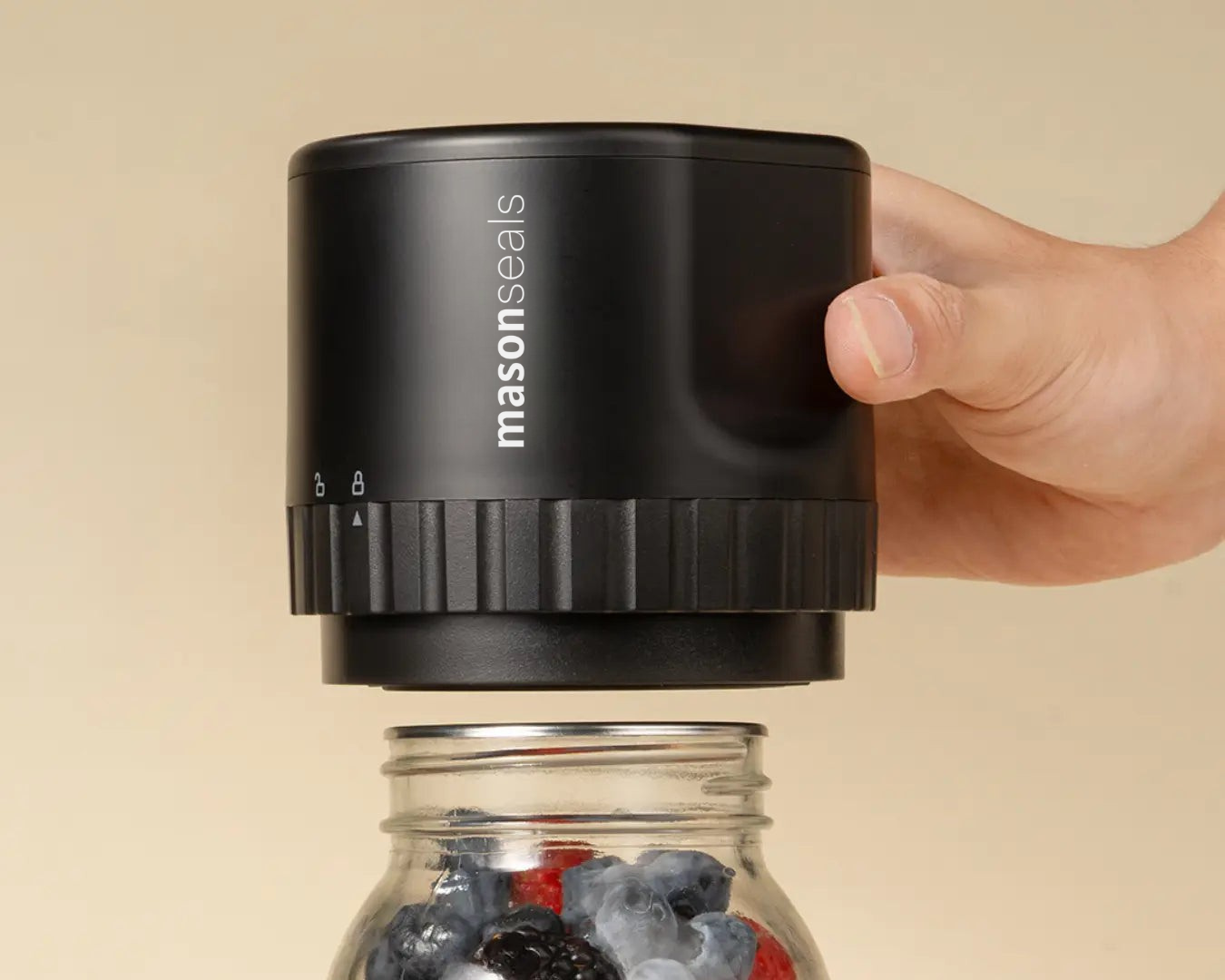 Hand holding a black mason jar sealer above a jar of berries.