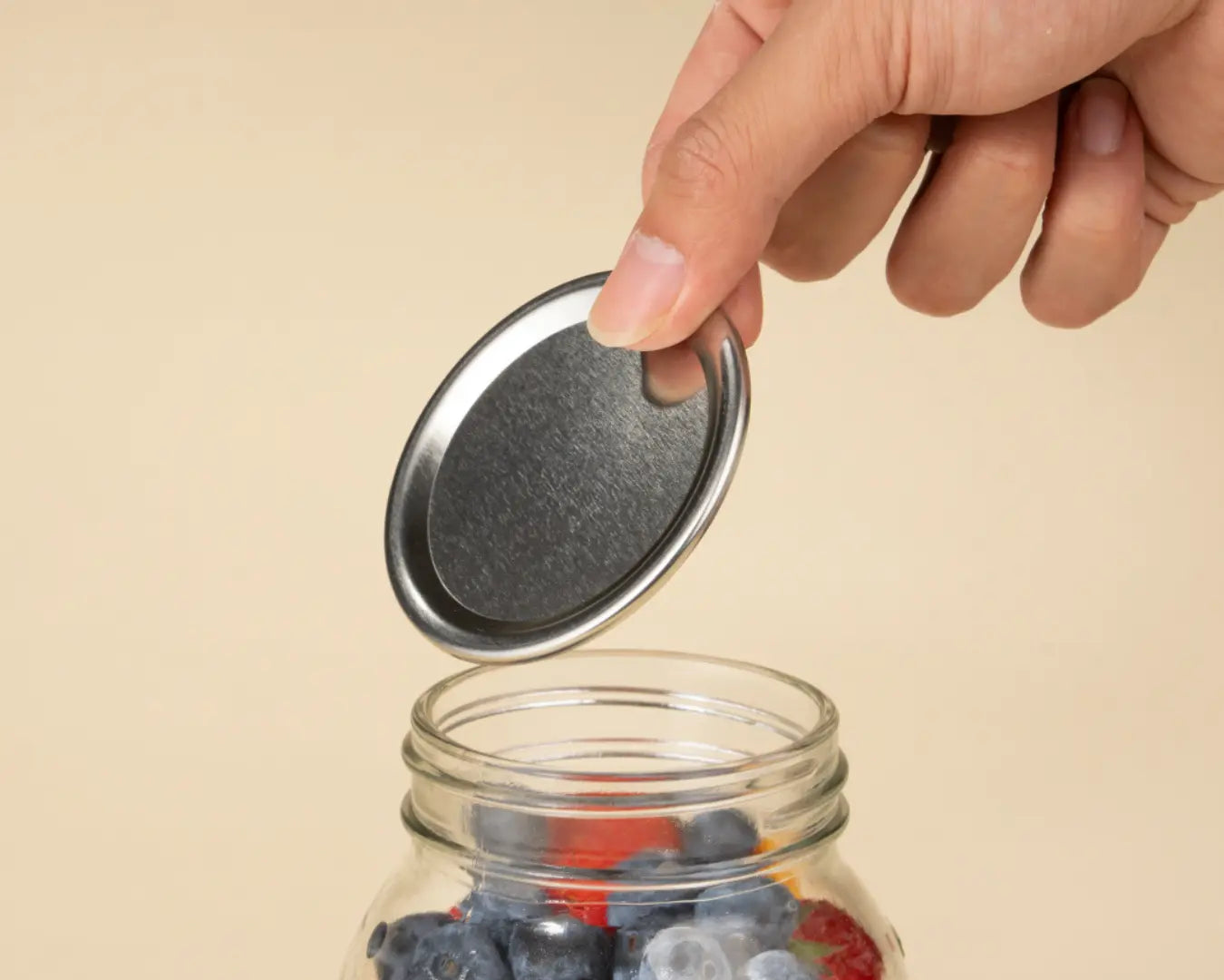 Hand placing lid on a jar filled with berries.