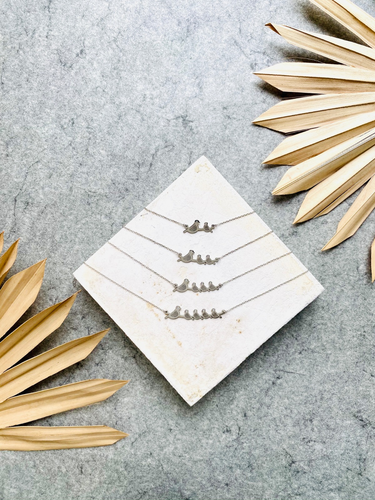 Gold bird necklace in a black jewelry box with a white lid nearby.