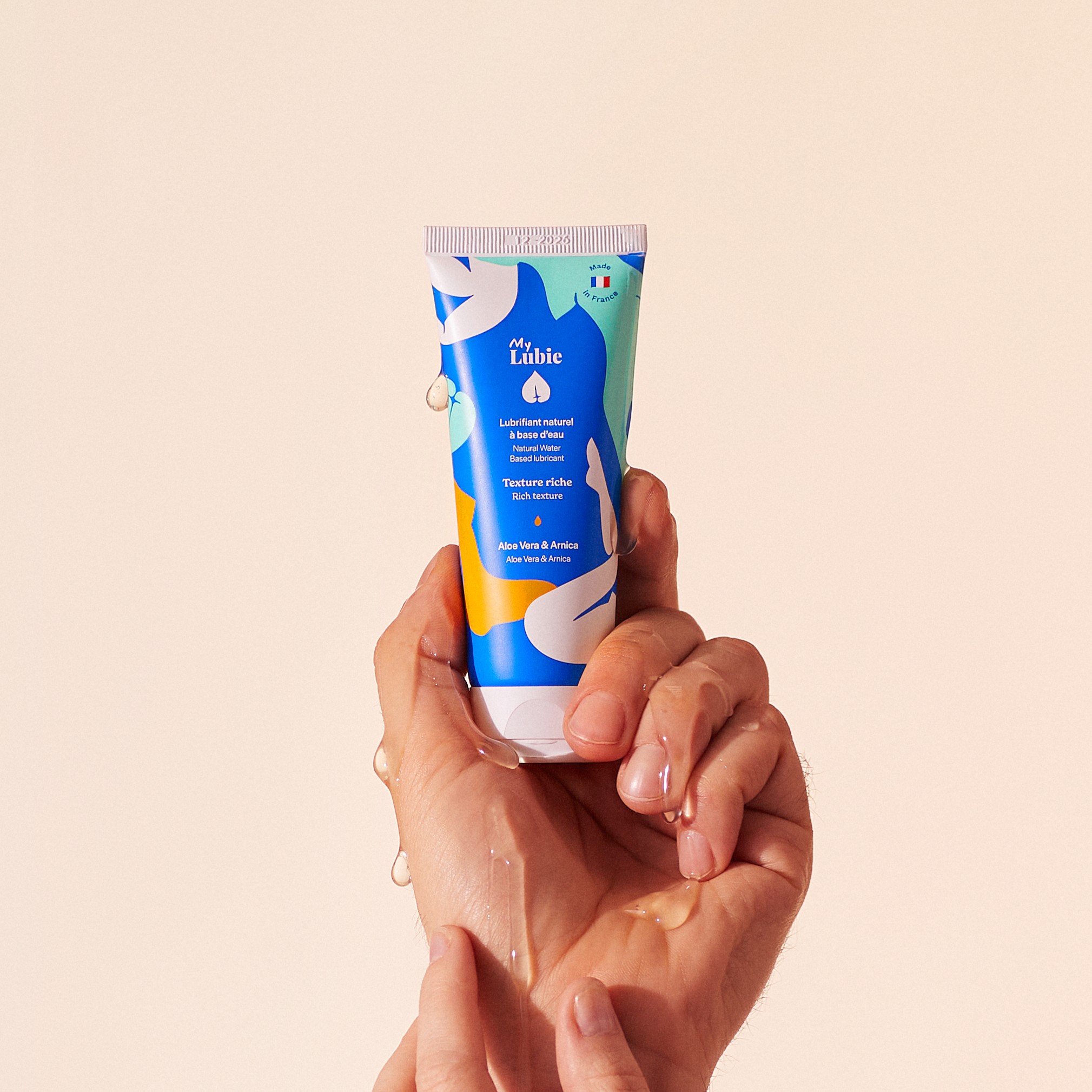 Hands holding a blue tube of lubricant with water droplets.