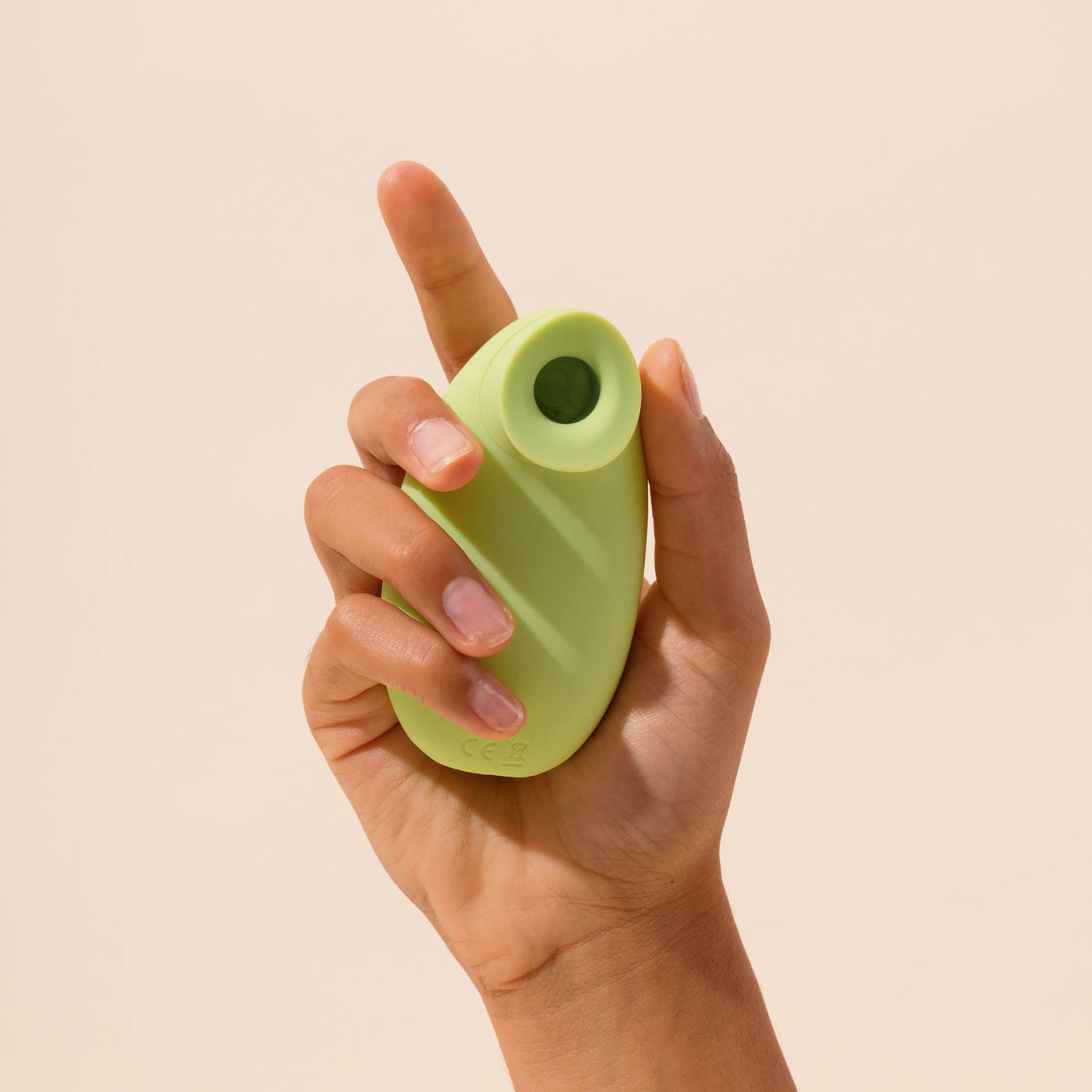 Hand holding a small green silicone device against a beige background.