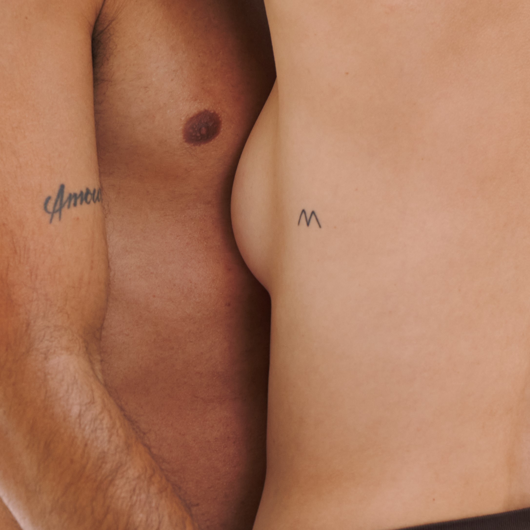Two tattooed torsos close together, one with 'Amour' tattoo.