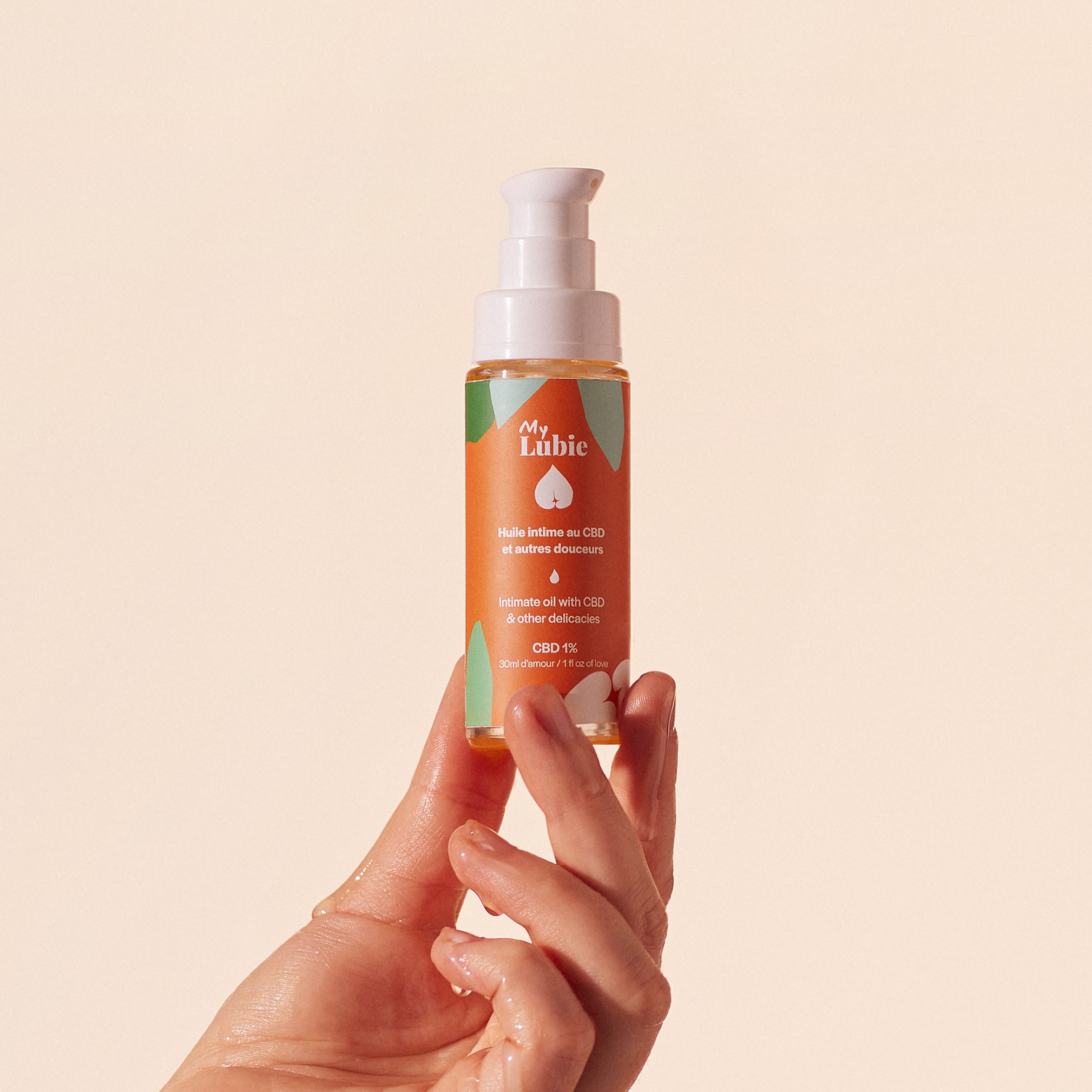 Hand holding a bottle of intimate oil with CBD against a plain background.