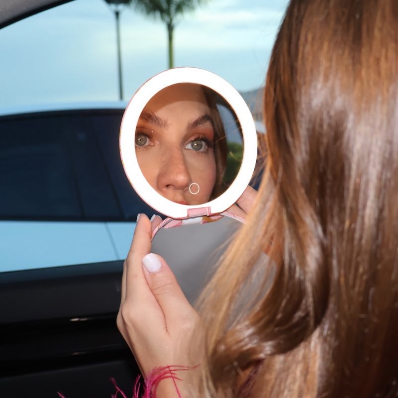 Woman looking into a round mirror with a car window reflection in the background.