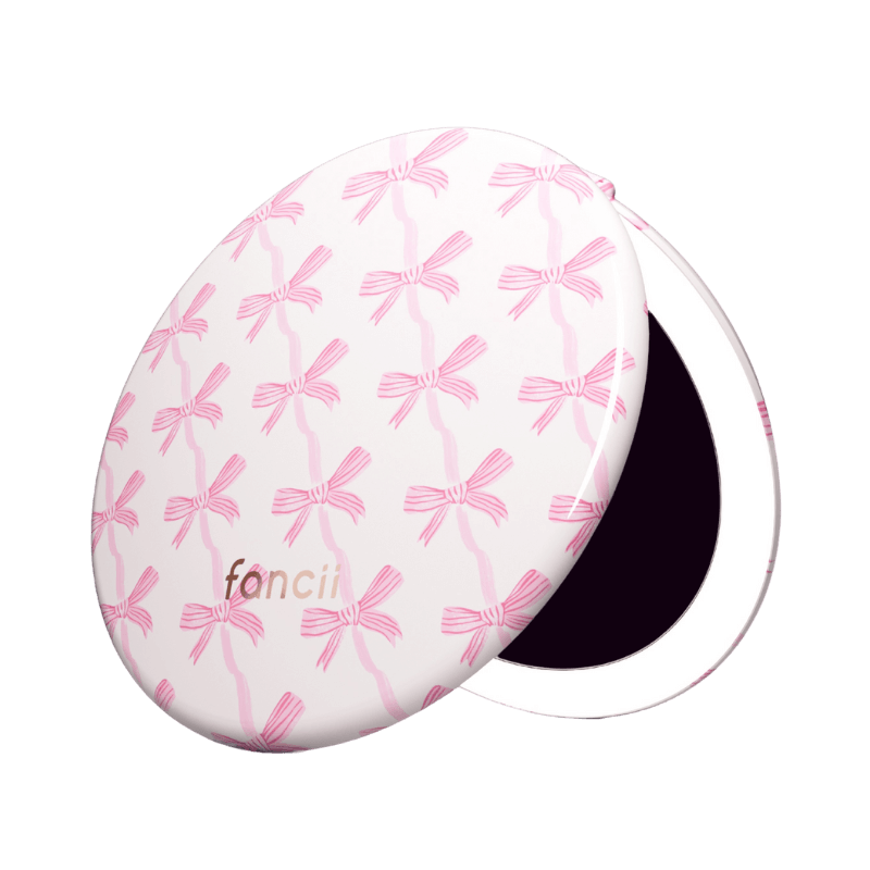Round compact mirror with pink bow pattern and 'fancii' text.