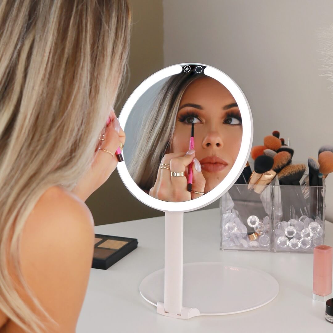 Person applying makeup in front of a lighted round mirror.