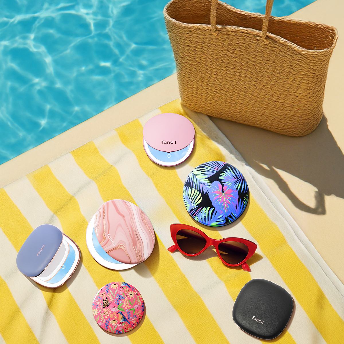 Colorful compact mirrors and red sunglasses on a striped towel by a pool.