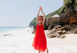 Person in red dress standing on a beach near rocks.