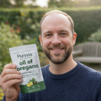 A smiling man in a blue sweater holds up a white pouch of Purevia oil of oregano.
