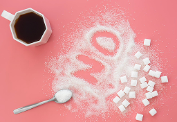 Coffee cup, sugar cubes, and spilled sugar spelling 'NO' on pink surface.