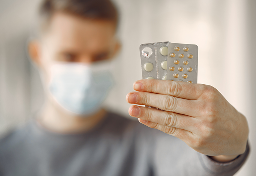 Person wearing a mask holding blister packs of pills.