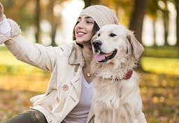 Woman and golden retriever taking a selfie in a park during autumn.