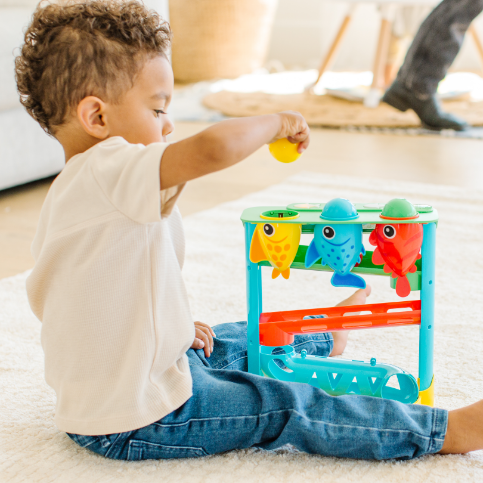 Child playing with a colorful fish-themed toy on a carpeted floor.
