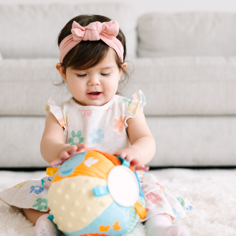 Baby playing with a colorful ball on a soft rug.