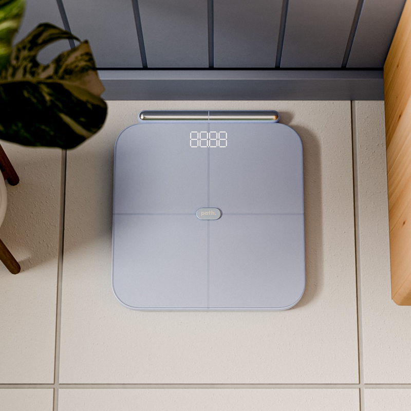 An overhead view of a light blue digital bathroom scale on a tiled floor.