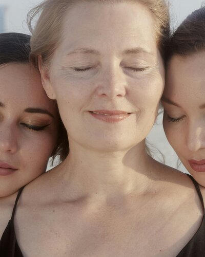 A close-up of three women with their eyes closed, their heads resting together.