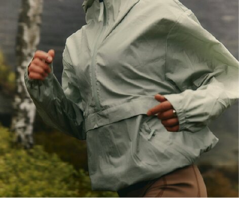 A person wearing a light green hooded jacket while running outdoors.