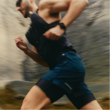 A man in athletic wear is shown in a motion-blurred profile shot as he runs past a rocky background.
