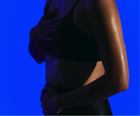 A close-up of a person's torso in a black top, with glistening skin against a blue background.