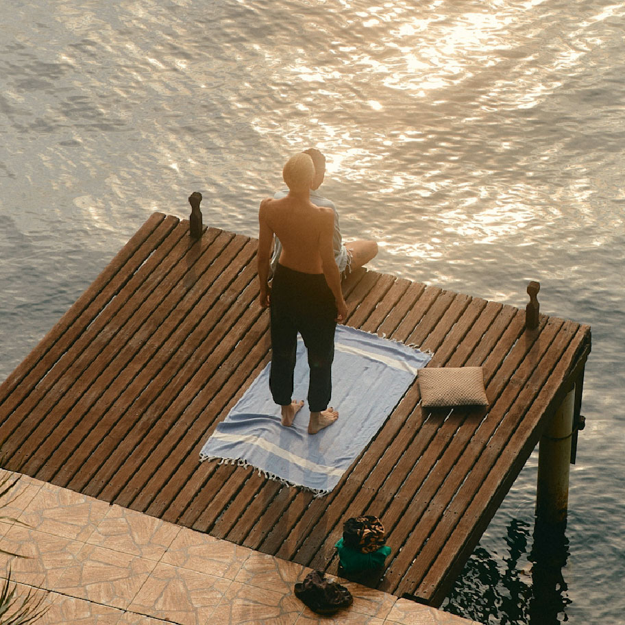 Two people seen from behind on a wooden dock over water as the sun sets.