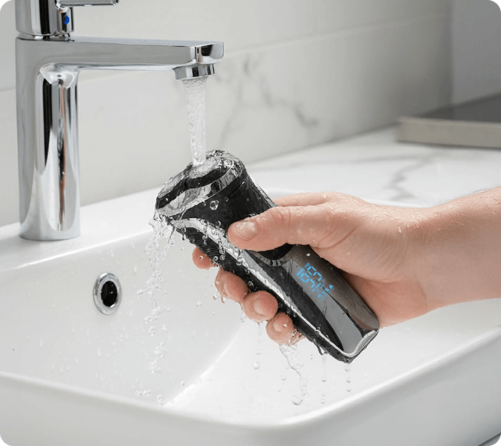 Hand rinsing a black electric shaver under a faucet in a sink.