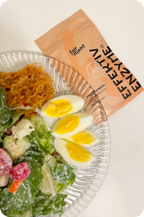 Plate with salad, boiled eggs, fermented vegetables, and enzyme supplement packet.